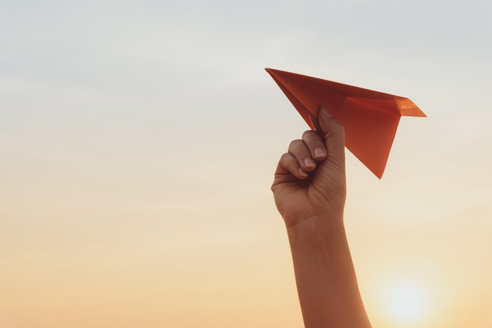 A hand launching a red paper plane into the sky